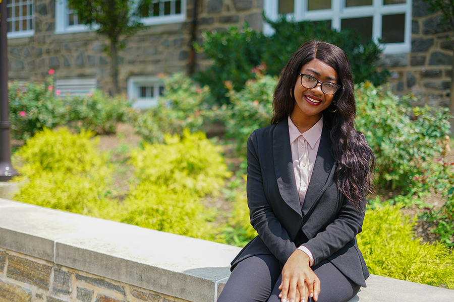 Nashae Prout sits on a stone wall on the MSU campus smiling.